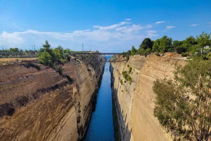 Schmaler blauer Wasserkanal zwischen hohen beigen Felsw&auml;nden, Br&uuml;cke oben, blauer Himmel mit Wolken, Vegetation an den R&auml;ndern