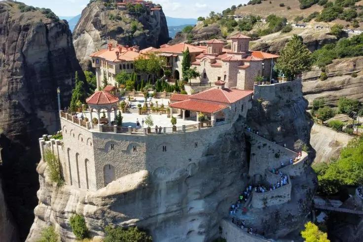 Steinerne Geb&auml;ude mit roten Ziegeld&auml;chern auf einem hohen, freistehenden Felsplateau; Treppen und Wege an der Felswand, sichtbare Menschen, umliegende Felsen und blauer Himmel