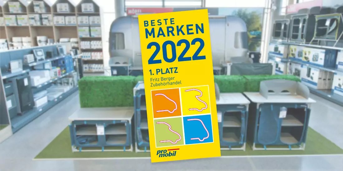 Gelbes Aufsteller-Schild mit dem Text "BESTE MARKEN 2022 1. PLATZ" vor mehreren grauen Kunststoffboxen mit Aussparungen auf gr&uuml;nem Untergrund, im Hintergrund Regale mit Produkten