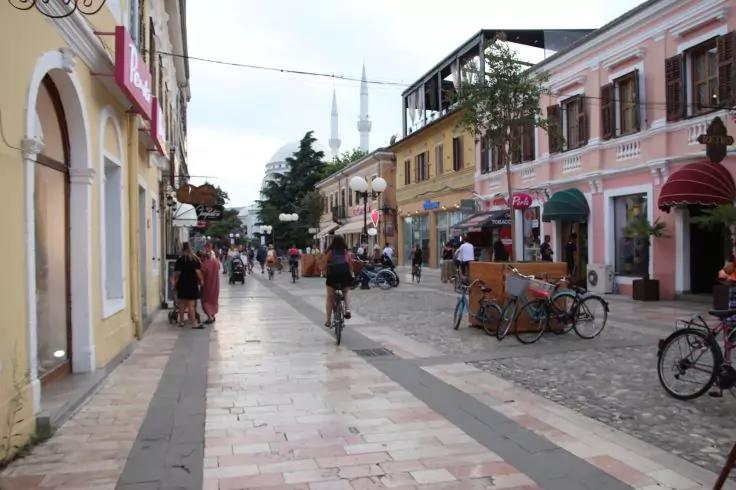 Gepflasterte Fußgängerstraße mit Menschen zu Fuß, einem Radfahrer, geparkten Fahrrädern, bunten Ladenfassaden an beiden Seiten und zwei Minaretten im Hintergrund