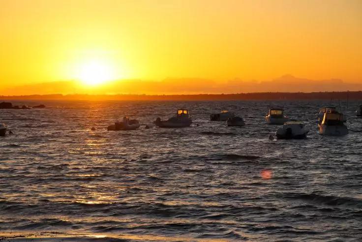 Sonnenuntergang &uuml;ber dem Meer, mehrere kleine Boote auf dem Wasser, Sonne knapp &uuml;ber dem Horizont, Lichtreflexe auf der Wasseroberfl&auml;che