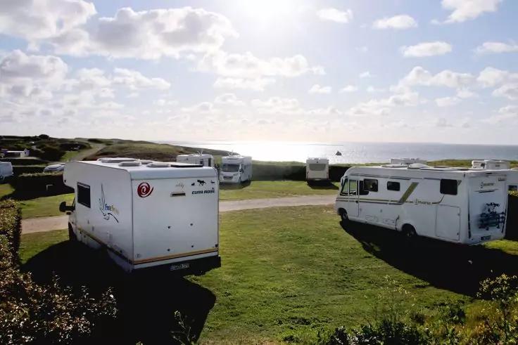 Mehrere Wohnmobile auf einer Grasfl&auml;che nahe der K&uuml;ste, Meer am Horizont, schmaler Weg, bew&ouml;lkter Himmel mit Sonne