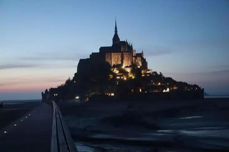 Beleuchtete befestigte Anlage auf einer felsigen Insel bei D&auml;mmerung, im Vordergrund ein Steg, umgeben vom Meer