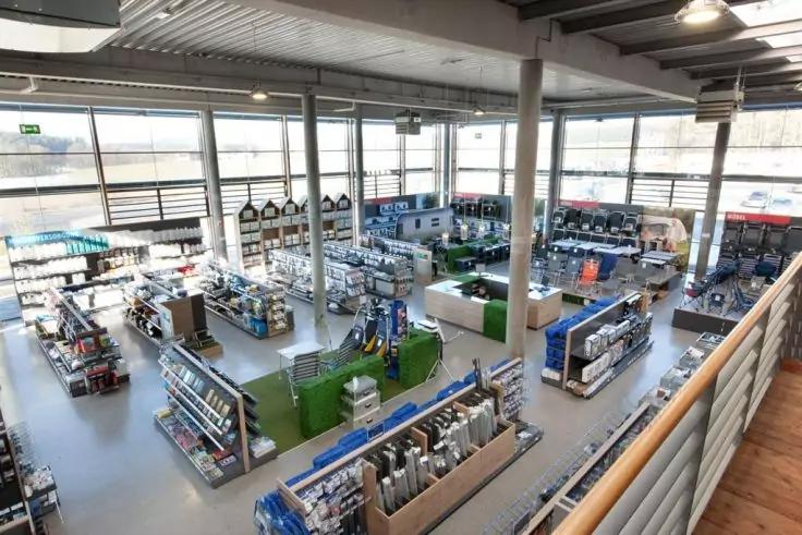 Großer heller Innenraum mit hohen Fenstern, Reihen von Regalen und Gängen, Stützsäulen, Deckenbeleuchtung und offener Empore