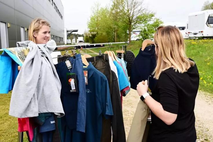 Zwei Frauen stehen an einer Kleiderstange im Freien und betrachten darauf h&auml;ngende Kleidung; im Hintergrund ein Geb&auml;ude und Fahrzeuge