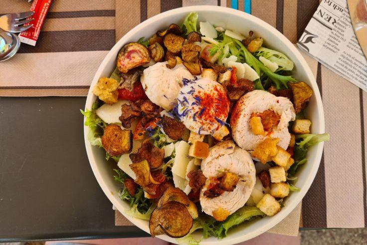 Salatsch&uuml;ssel mit Blattsalat, ger&ouml;steten Kartoffelscheiben, Brotw&uuml;rfeln, hellen aufgerollten Scheiben, d&uuml;nnen K&auml;sescheiben und einer wei&szlig;en Kugel mit rotem Gew&uuml;rz in der Mitte