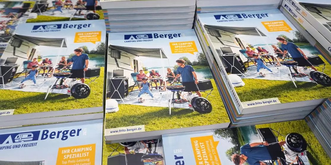 Gestapelte Prospekte mit Berger-Logo; Titelseite zeigt mehrere Personen auf einer Wiese neben einer Markise, Klappst&uuml;hlen, einem Tisch und einem runden Ger&auml;t auf R&auml;dern; orangefarbene Aufkleber