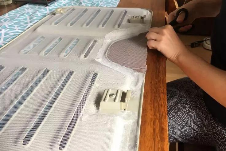 H&auml;nde schneiden mit einer Schere den Rand eines wei&szlig;en Stoffbezugs mit l&auml;nglichen &Ouml;ffnungen und zwei Kunststoffclips, Bezug liegt auf einem Holztisch