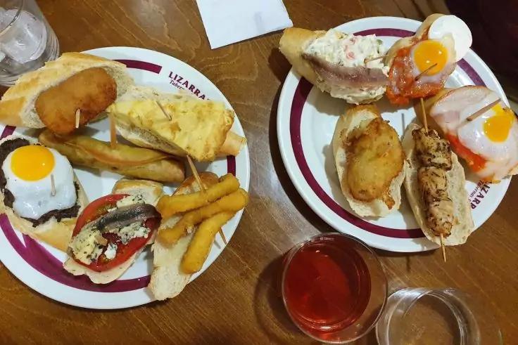 Zwei Teller mit aufgeschnittenen Br&ouml;tchen mit Spiegelei, Pommes, paniertem Snack und zwei Gl&auml;sern auf einem Holztisch