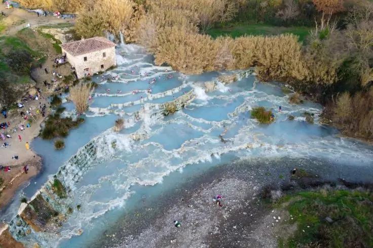 Luftaufnahme von terrassenf&ouml;rmigen, hellblauen Wasserbecken mit kleinen Kaskaden, einem Steinhaus links, Menschen am Ufer und bewachsenen Uferbereichen