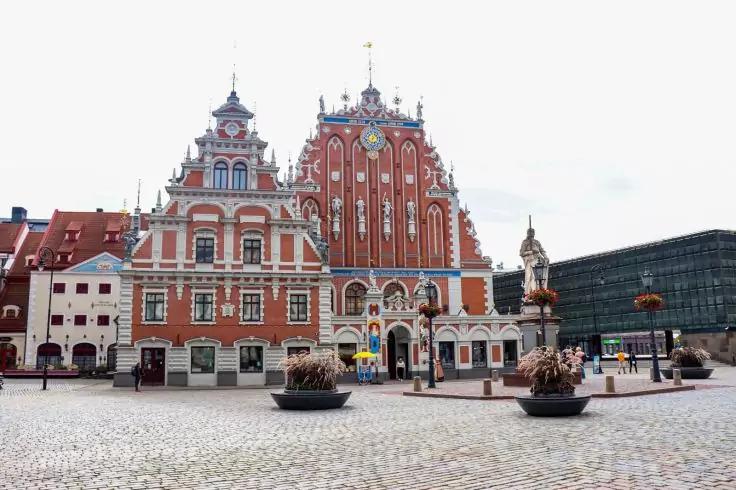 Rote, reich verzierte Backsteinfassade mit Giebeln an einem gepflasterten Platz, Blumk&uuml;bel im Vordergrund