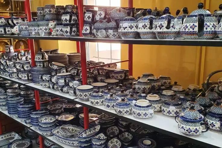 Regale mit blau-wei&szlig; gemustertem Geschirr auf mehreren Ebenen; Schalen, Teller, Tassen und Deckelschalen; rote Regalstreben, gelbe Wand und Fenster im Hintergrund