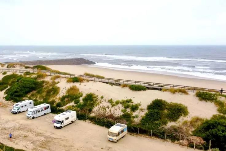 Meer mit Wellen, Sandd&uuml;nen, ein h&ouml;lzerner Steg und mehrere Wohnmobile am Strand