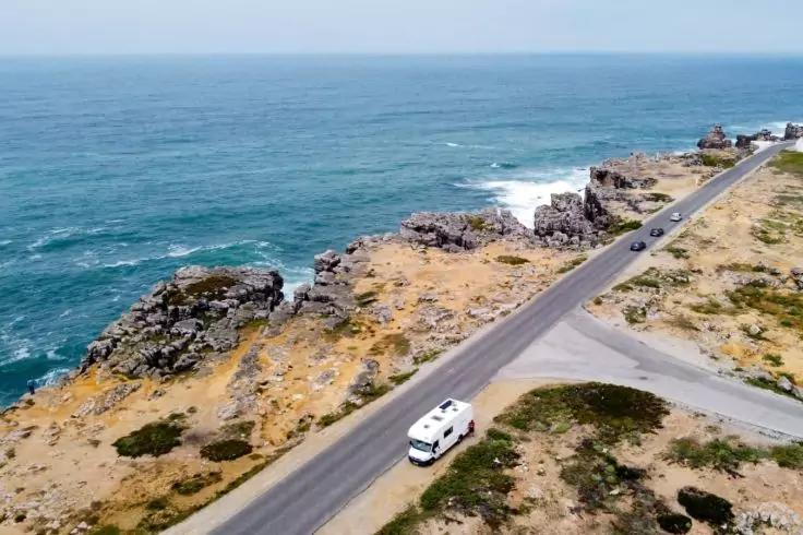 Wei&szlig;er Lieferwagen auf einer K&uuml;stenstra&szlig;e neben felsiger K&uuml;ste und offenem Meer