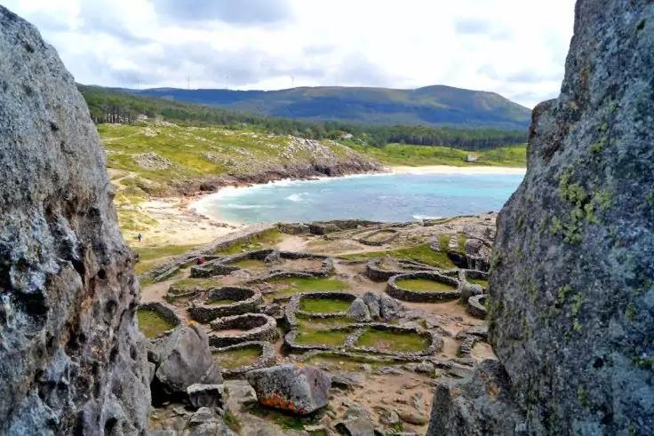 Blick durch Fels&ouml;ffnung auf kreisf&ouml;rmige Steinstrukturen, Strand, Meer und H&uuml;gel
