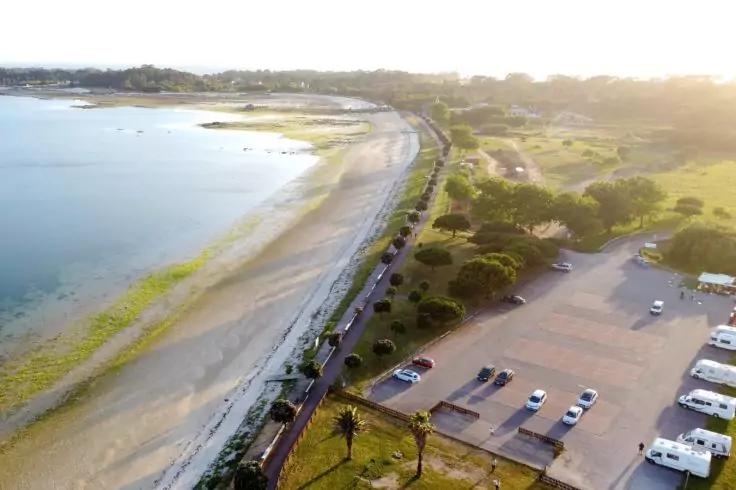 Luftaufnahme einer K&uuml;ste mit Sandstrand, Meer, Parkpl&auml;tzen und Wohnmobilen