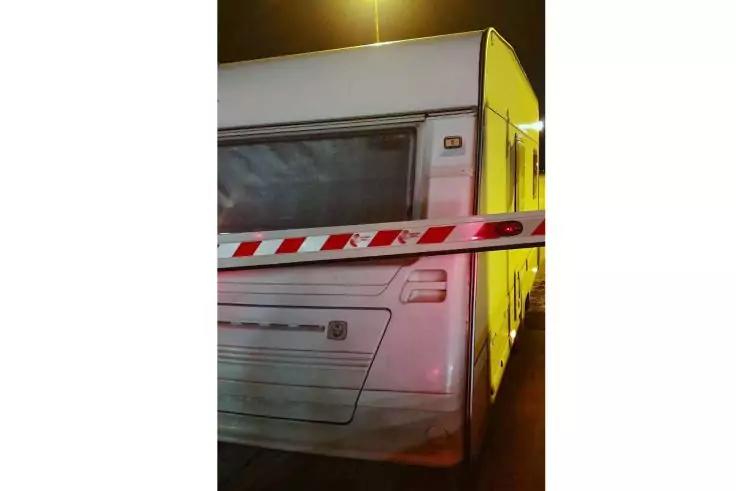 R&uuml;ckseite eines wei&szlig;en Wohnwagens, quer davor rot-wei&szlig; gestreiftes Absperrband, Nachtaufnahme mit Stra&szlig;enlaterne