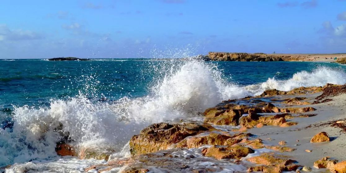 Brandung bricht an einer felsigen K&uuml;ste, Meereschaum und blaues Wasser unter klarem Himmel