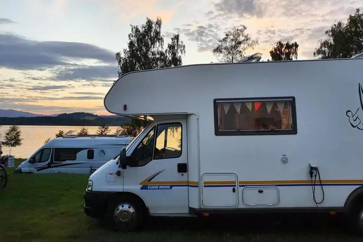 Wei&szlig;es Wohnmobil am Ufer, im Hintergrund weiteres Wohnmobil, See, B&auml;ume, H&uuml;gel, Abendhimmel