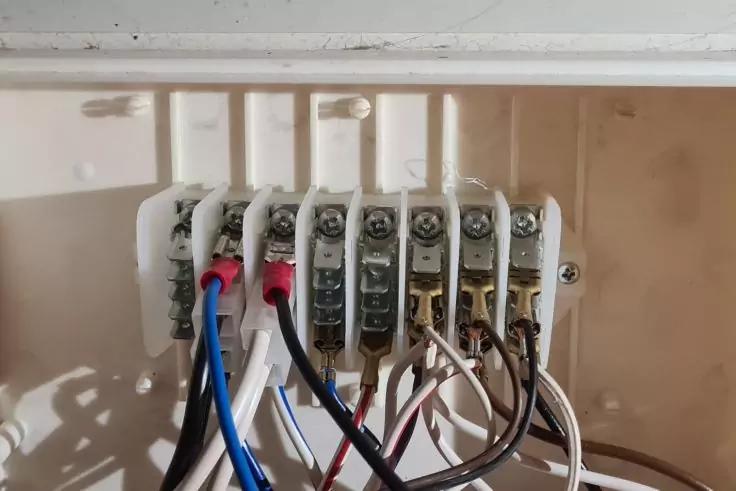 Kunststoff-Klemmenleiste mit sechs Schraubklemmen und daran angeschlossenen blauen, roten, schwarzen, braunen und weißen Kabeln in einem weißen Gehäuse