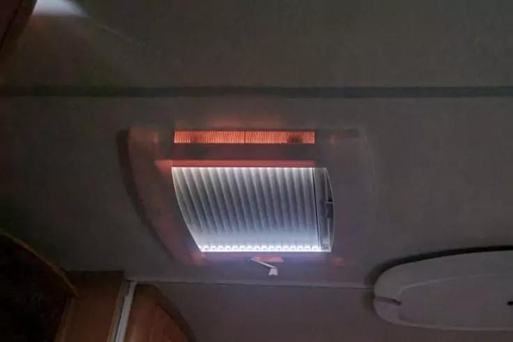 Rechteckige Decken&ouml;ffnung mit gestreifter Jalousie, LED-Licht darunter und Zugband; rundes Deckelpanel und Holzkante sichtbar