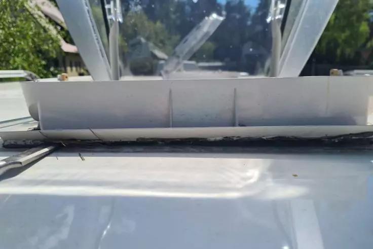 Ge&ouml;ffnetes Dachfenster mit Glas, Metallrahmen und Dichtungsmasse; im Hintergrund B&auml;ume und blauer Himmel