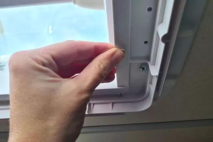 Hand h&auml;lt kleinen wei&szlig;en Stift am Rahmen eines Dachfensters; blauer Himmel durch das Glas sichtbar