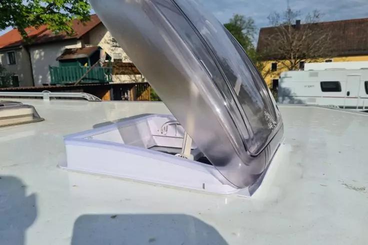 Ge&ouml;ffnete, transluzente Dachluke auf wei&szlig;em Dach; im Hintergrund H&auml;user, B&auml;ume und ein geparkter Wohnwagen