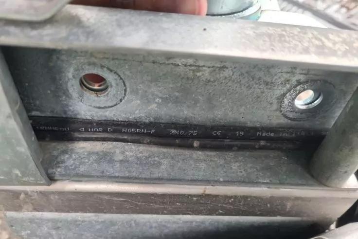 Nahaufnahme eines Metalltr&auml;gers mit zwei runden Bohrl&ouml;chern; in einer Nut liegt ein schwarzes Kabel; oben links ist ein Finger sichtbar