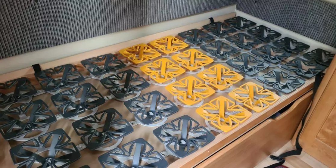 Mehrere quadratische Gittereins&auml;tze in Schwarz und Gelb nebeneinander auf einer Holzarbeitsfl&auml;che; rechts unten ein Holzschrank, im Hintergrund eine vertikal gestreifte Wand