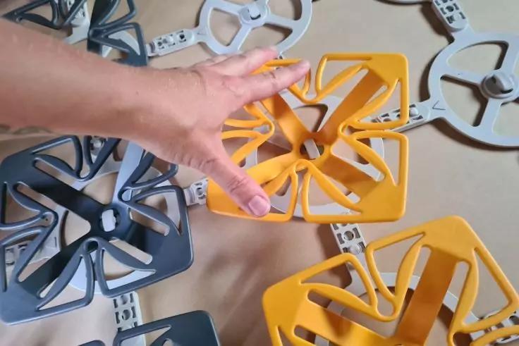 Hand &uuml;ber einem gelben sternf&ouml;rmigen Kunststoffteil, daneben mehrere graue und gelbe Kunststoffteile auf hellem Untergrund