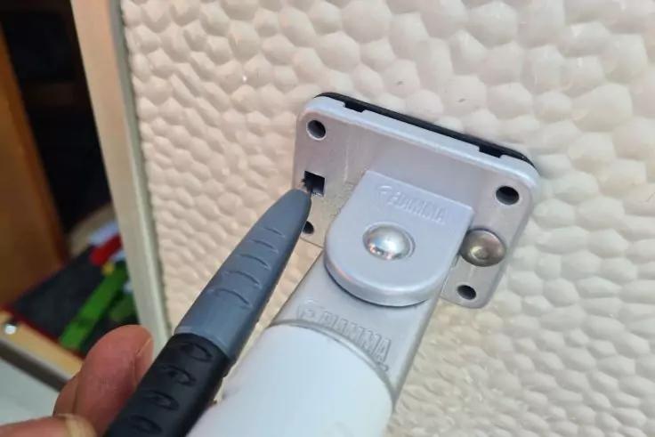 Hand h&auml;lt einen grauen Schraubendreher an einer Schraube in einer wei&szlig;en Halterung an einer strukturierten wei&szlig;en Wand