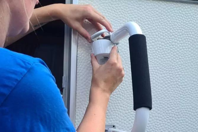 Teilansicht einer Person in blauem Shirt, H&auml;nde halten einen wei&szlig;en Kunststoffverbinder an einen gebogenen wei&szlig;en Griff mit schwarzem Schaumstoffbezug vor einer hellen, strukturierten Wand