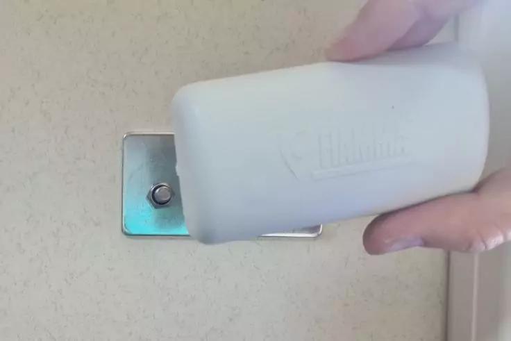 Hand h&auml;lt wei&szlig;en Kunststoffk&ouml;rper &uuml;ber rechteckige Metallplatte an heller Wand