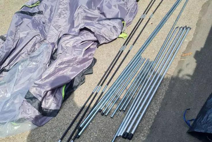 Zusammengelegter grauer Stoff mit gr&uuml;nem Saum und mehrere nebeneinander liegende silberne Metallstangen auf Asphalt; Schatten am rechten Bildrand