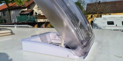 Aufgeklappte transparente Kunststoff-Dachluke auf wei&szlig;er Dachfl&auml;che; H&auml;user und Wohnwagen im Hintergrund