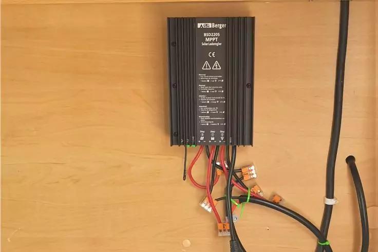 Schwarzes elektronisches Gerät mit Aufschriften, an einer Holzplatte befestigt, mehrere farbige Kabel und Steckverbinder darunter