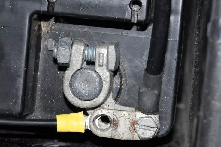 Metall-Batterieklemme auf Batteriepol, dickes schwarzes Kabel, gelber isolierter Kabelschuh, Schraube und schwarzes Kunststoffgehäuse