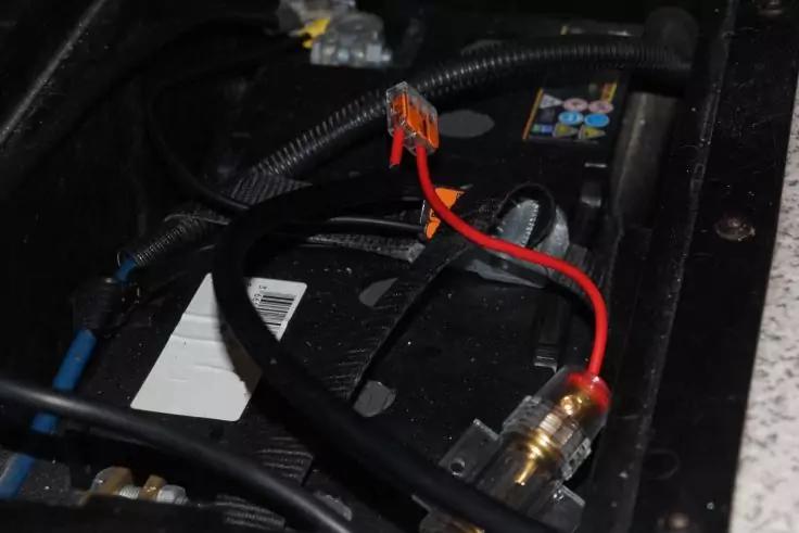 Schwarze Batterie mit roten und schwarzen Kabeln und Steckverbindern, umgeben von Kabeln und einem schwarzen Rahmen