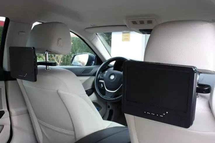 Innenraum eines Autos mit hellen Ledersitzen, Lenkrad, Armaturenbrett und zwei Bildschirmen an den R&uuml;ckseiten der Vordersitze