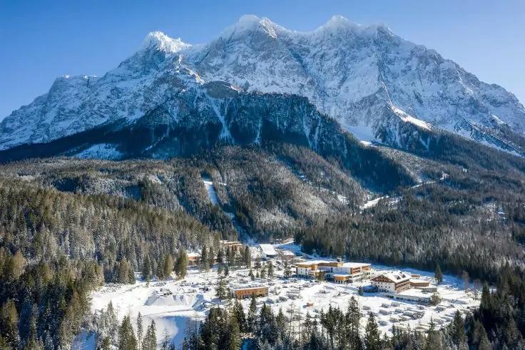 Schneebedeckte Berggipfel &uuml;ber einem verschneiten Dorf und Nadelwald, blauer Himmel