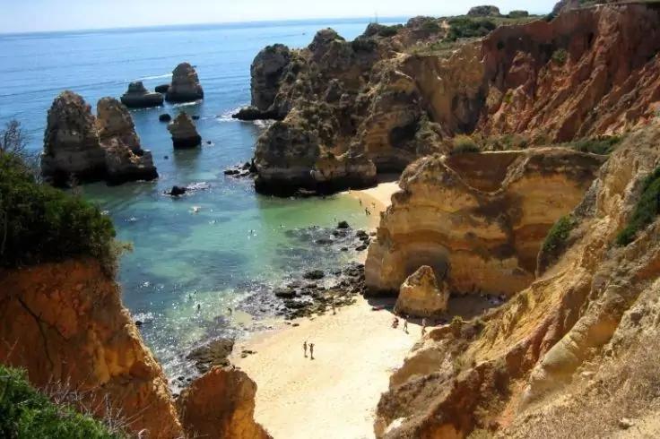 Sandstrand in einer kleinen Bucht zwischen steilen Felsklippen, t&uuml;rkisblaues Meer, zwei Personen am Strand