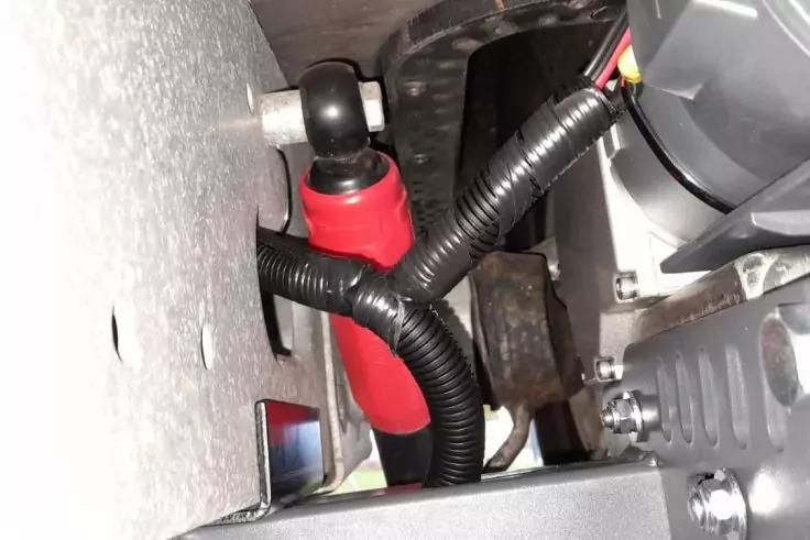 Nahaufnahme von Metallblech, einer roten isolierten Kabelverbindung, schwarzem Wellschlauch und einer Schraube