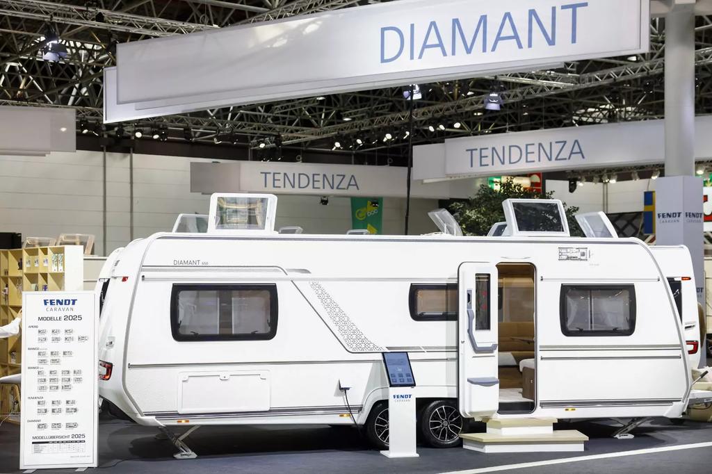 Wei&szlig;er Wohnwagen mit ge&ouml;ffneter T&uuml;r auf einer Messehalle, dar&uuml;ber Banner mit Schriftzug 'DIAMANT' und 'TENDENZA', Informationsst&auml;nder links