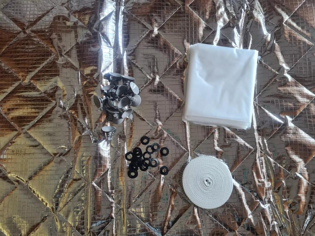 Silberfarbenes, gestepptes, reflektierendes Untergrundmaterial mit einem zerkn&uuml;llten silbernen Folienst&uuml;ck, einem gefalteten wei&szlig;en Tuch, mehreren kleinen schwarzen Ringen und einer wei&szlig;en Rolle