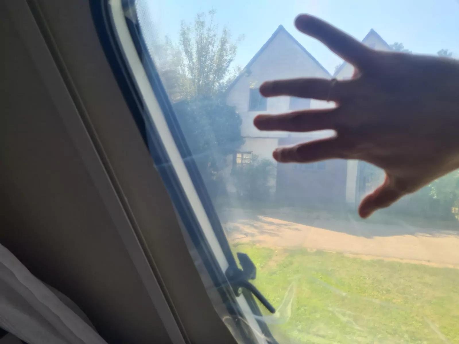 Hand vor leicht ge&ouml;ffnetem Dachfenster, im Hintergrund Haus, Rasen und Baum