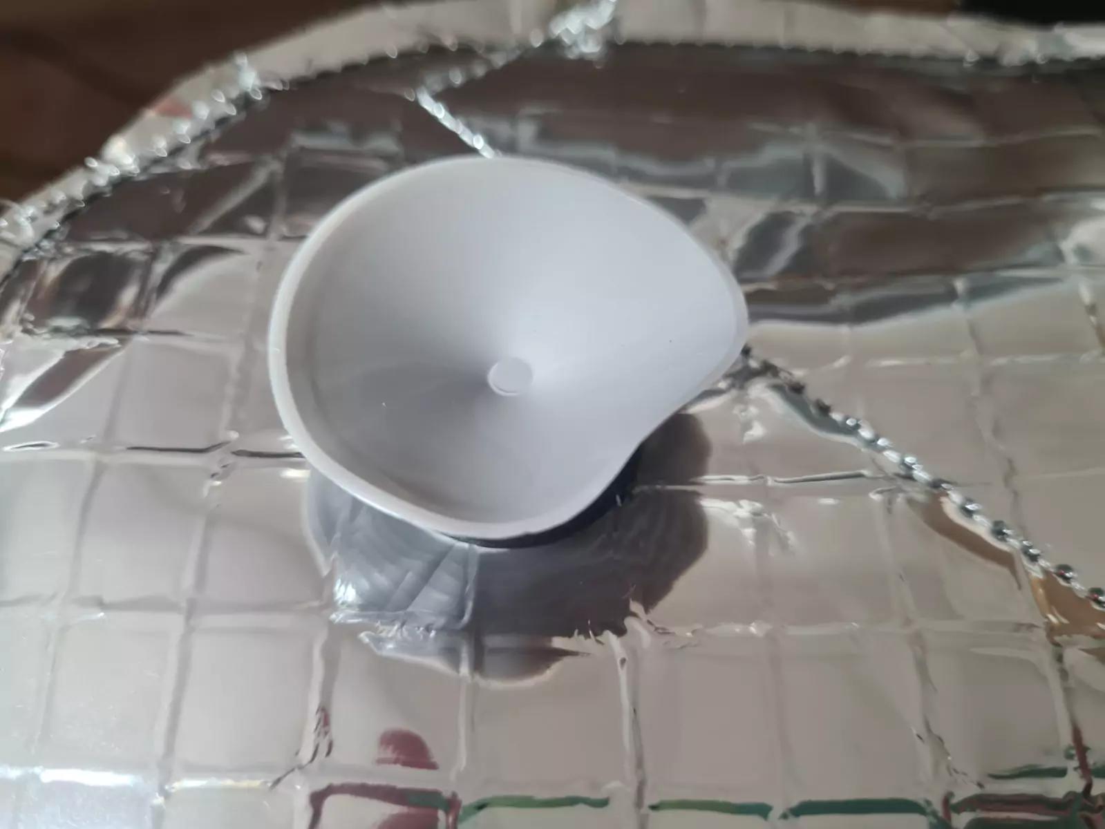 Kleiner wei&szlig;er Kunststoffbecher mit unregelm&auml;&szlig;igem Rand auf zerknitterter silberner, reflektierender Folie