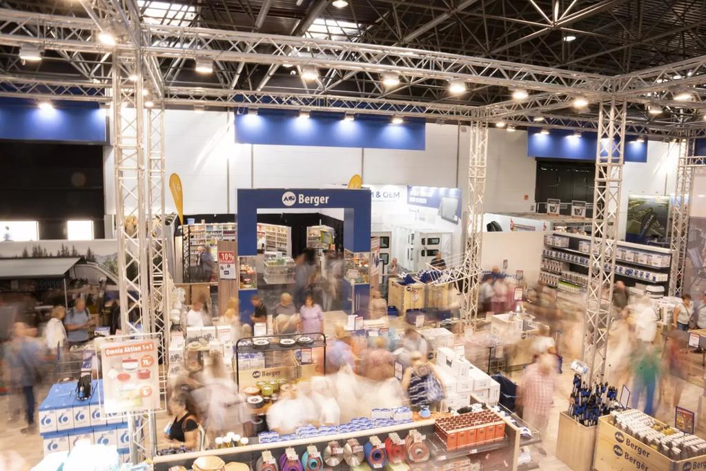 Gro&szlig;e Halle mit St&auml;nden, Produktregalen und vielen verschwommenen Personen unter sichtbaren Metalltr&auml;gern und Deckenbeleuchtung