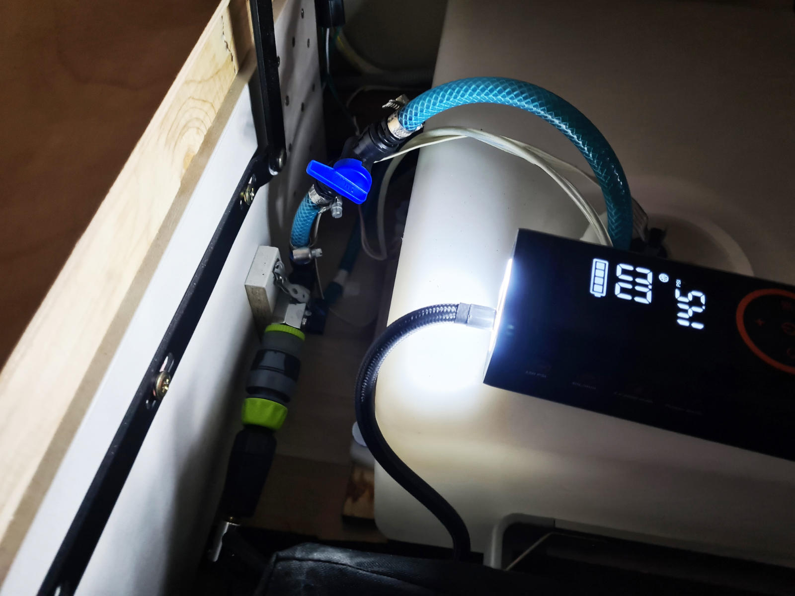 Wei&szlig;er zylindrischer Beh&auml;lter mit angeschlossenen Schl&auml;uchen, blauem Absperrhahn und schwarzem digitalen Display mit wei&szlig;en Zahlen; Holzrand links