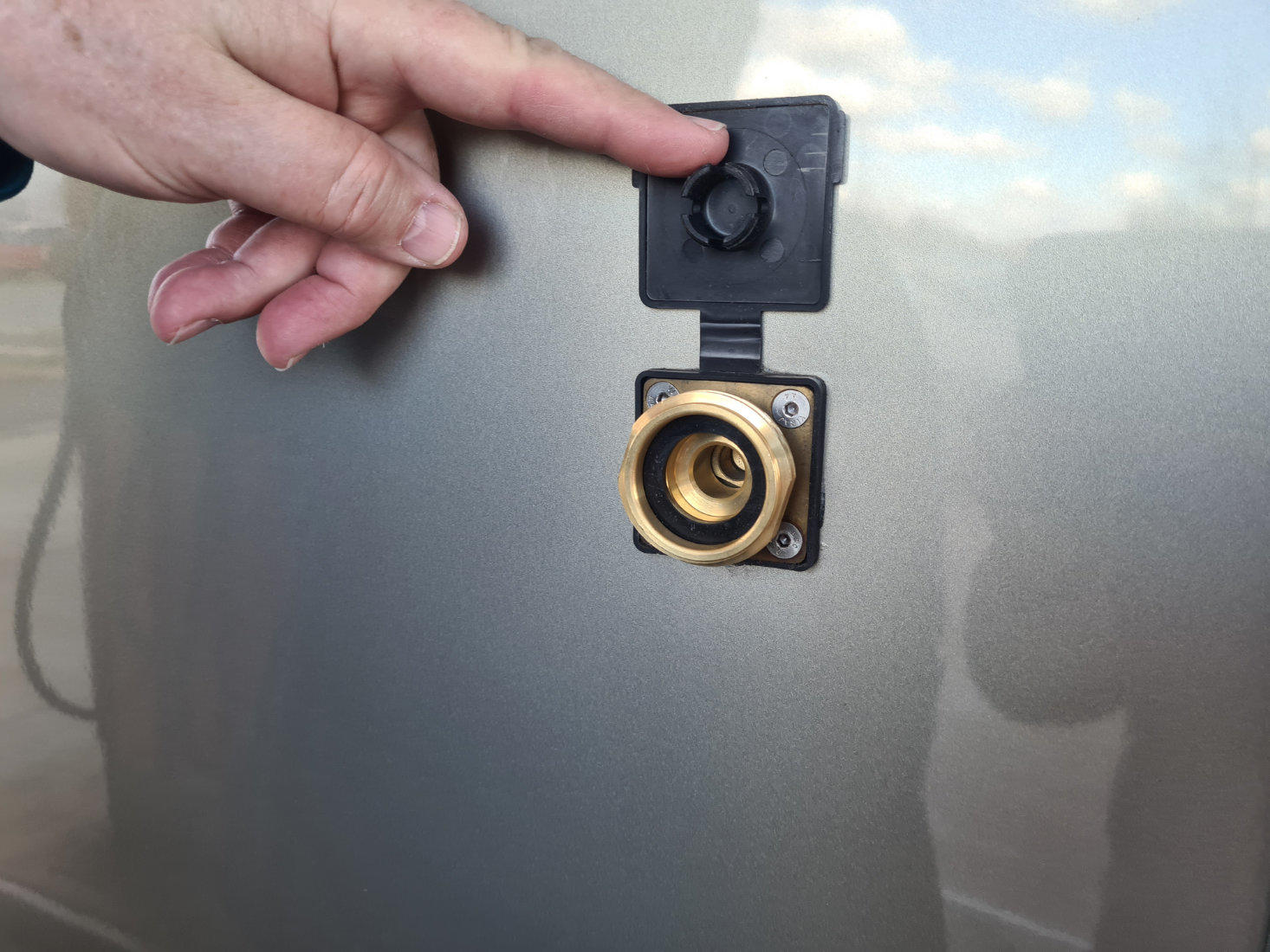 Hand hebt schwarzen Klappdeckel über rundem, messingfarbenem Anschluss an silberner Fahrzeugkarosserie